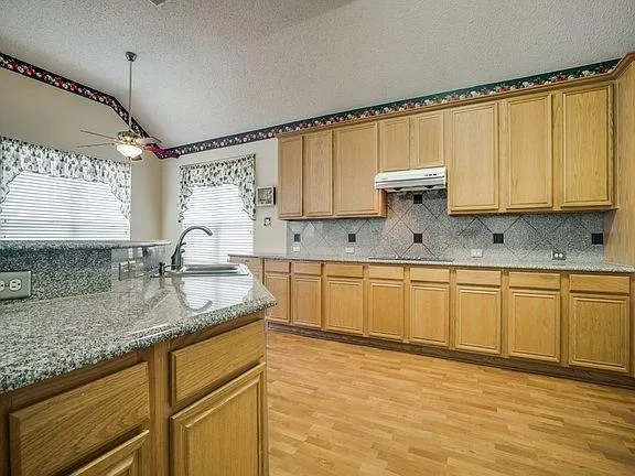 a kitchen with granite countertop a sink a stove cabinets and wooden floor