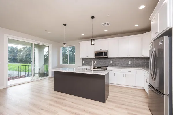 a kitchen with stainless steel appliances granite countertop a refrigerator a sink dishwasher a stove and white countertops with wooden floor