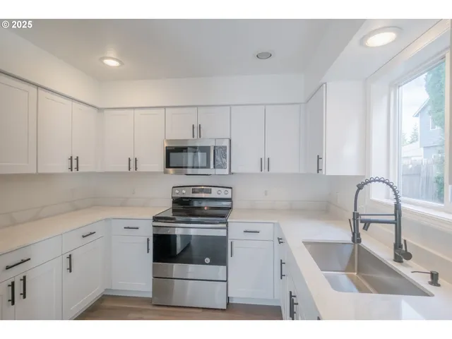 a kitchen with stainless steel appliances kitchen island white cabinets a sink a stove a refrigerator and white cabinets