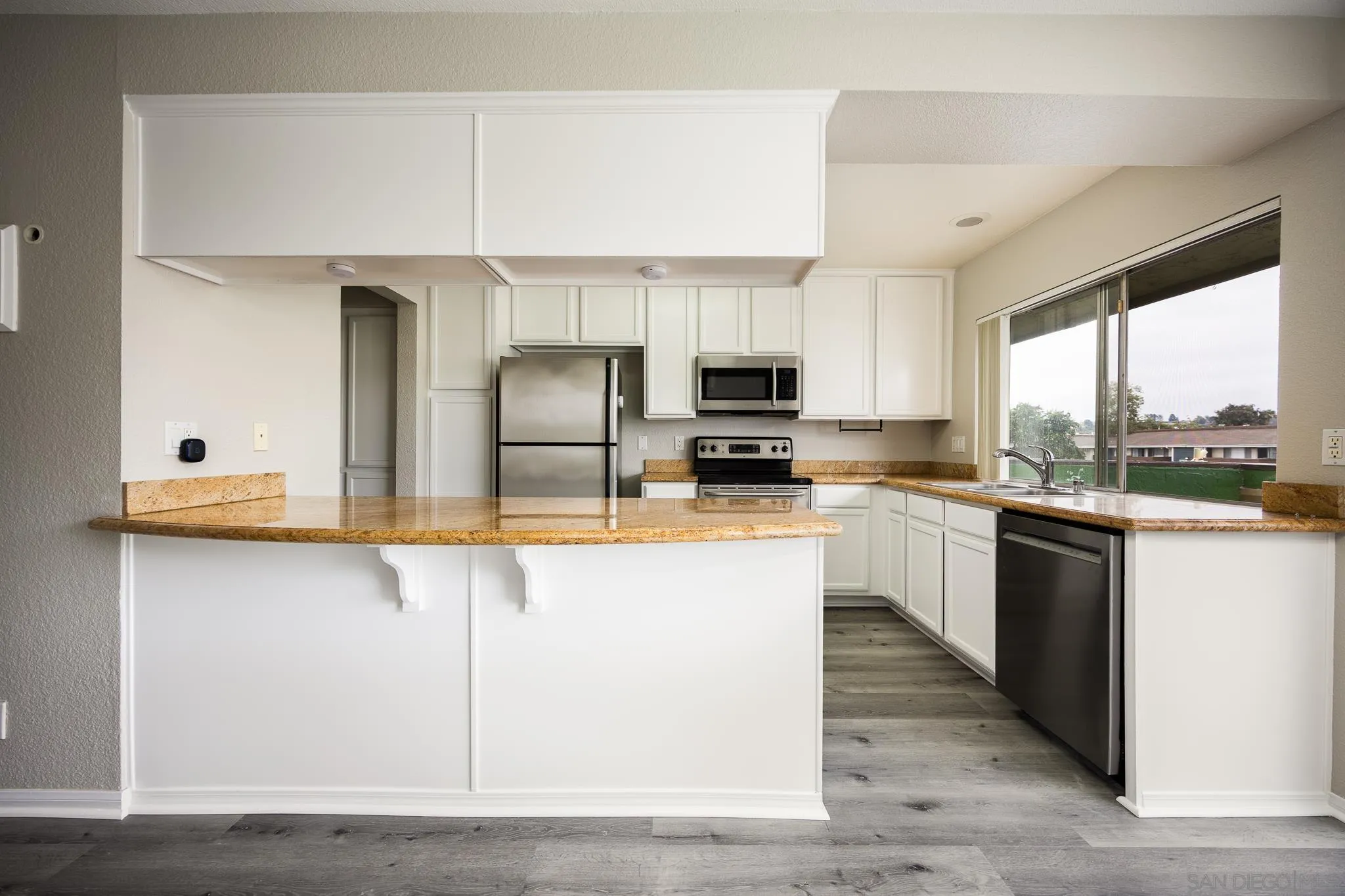 615 Fredricks Avenue, Unit 134 Oceanside, CA 92058 - Photo 6 of 40 a large kitchen with kitchen island granite countertop a stove a sink a refrigerator and white cabinets with wooden floor