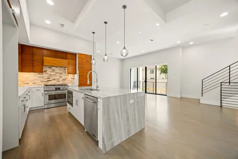 a kitchen with stainless steel appliances granite countertop a stove top oven a sink dishwasher a refrigerator and a dining table with wooden floor