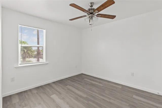 an empty room with wooden floor fan and windows