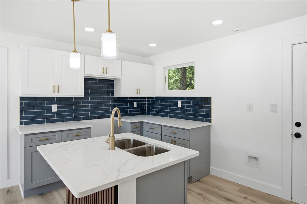 905 East Shaw Street Fort Worth, TX 76110 - Photo 9 of 19 Kitchen featuring a central island with dual basin sink, white cabinetry, blue subway tile backsplash, light-toned wood-finish flooring, and recessed lighting
