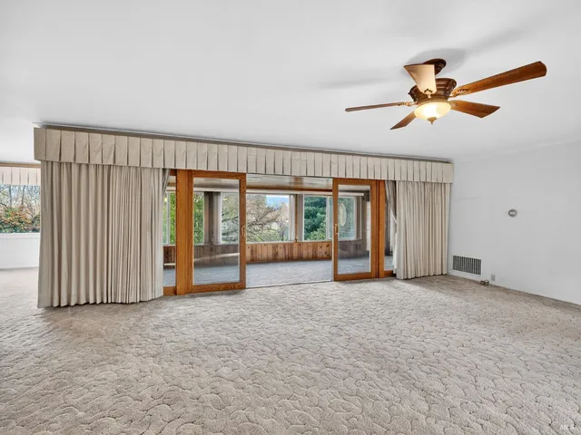 an empty room with ceiling fan and windows