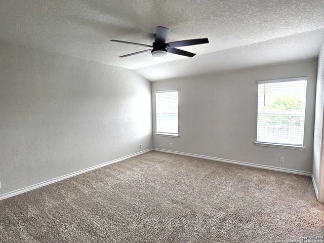 an empty room with wooden floor ceiling fan and windows