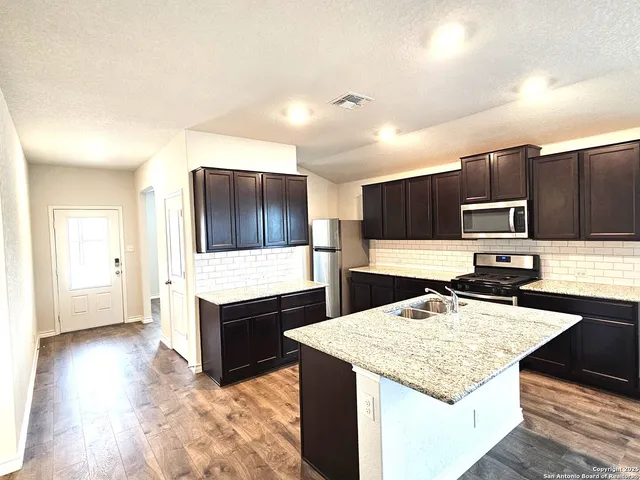 a kitchen with stainless steel appliances kitchen island granite countertop a stove refrigerator and cabinets