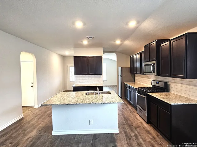 a large kitchen with stainless steel appliances a large counter top and wooden floors