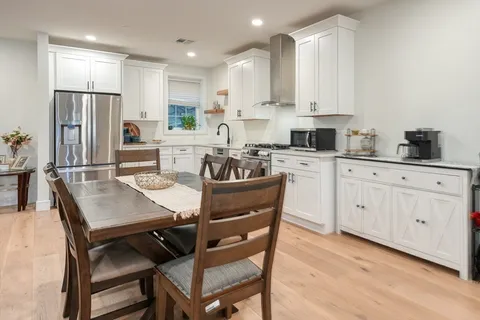 a kitchen with stainless steel appliances granite countertop a dining table chairs refrigerator and cabinets