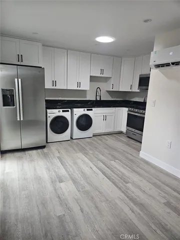 a kitchen with stainless steel appliances granite countertop a stove a refrigerator a sink and white cabinets with wooden floor