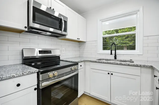 a kitchen with stainless steel appliances white cabinets granite counter tops and a window