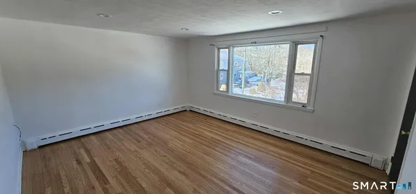 a view of an empty room with wooden floor and a window