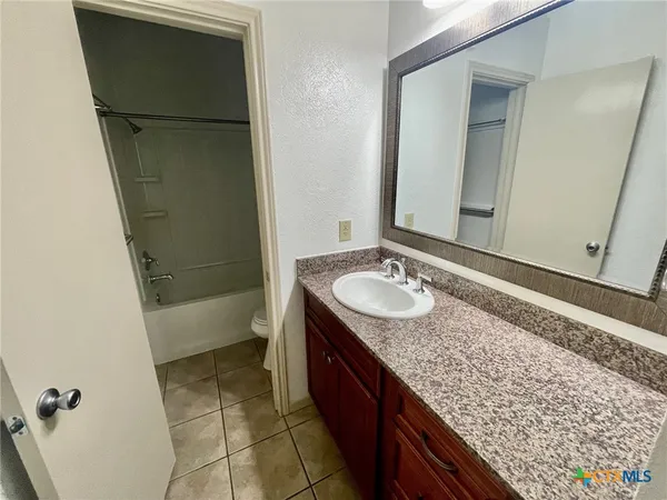 a bathroom with a granite countertop sink and mirror with bathtub
