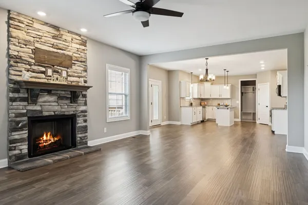 a view of a livingroom with a fireplace a ceiling fan and a kitchen view