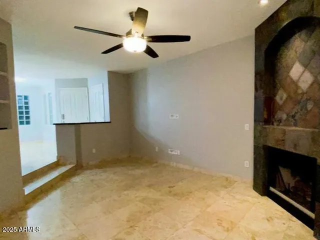 a view of an empty room with a fireplace and a ceiling fan