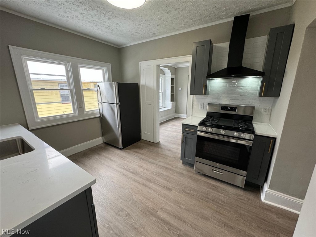 3333 Berea Road Cleveland, OH 44111 - Photo 15 of 34 Kitchen featuring light hardwood / wood-style floors, tasteful backsplash, wall chimney exhaust hood, appliances with stainless steel finishes, and a textured ceiling