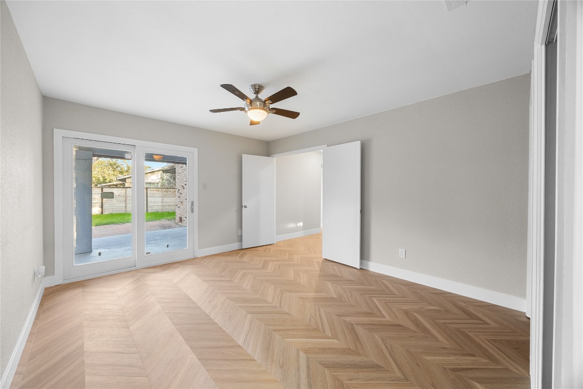 11714 Buckingham Road Austin, TX 78759 - Photo 18 of 35 Primary bedroom overlooking backyard with ceiling fan, tall baseboards and chevron / herringbone pattern floors.