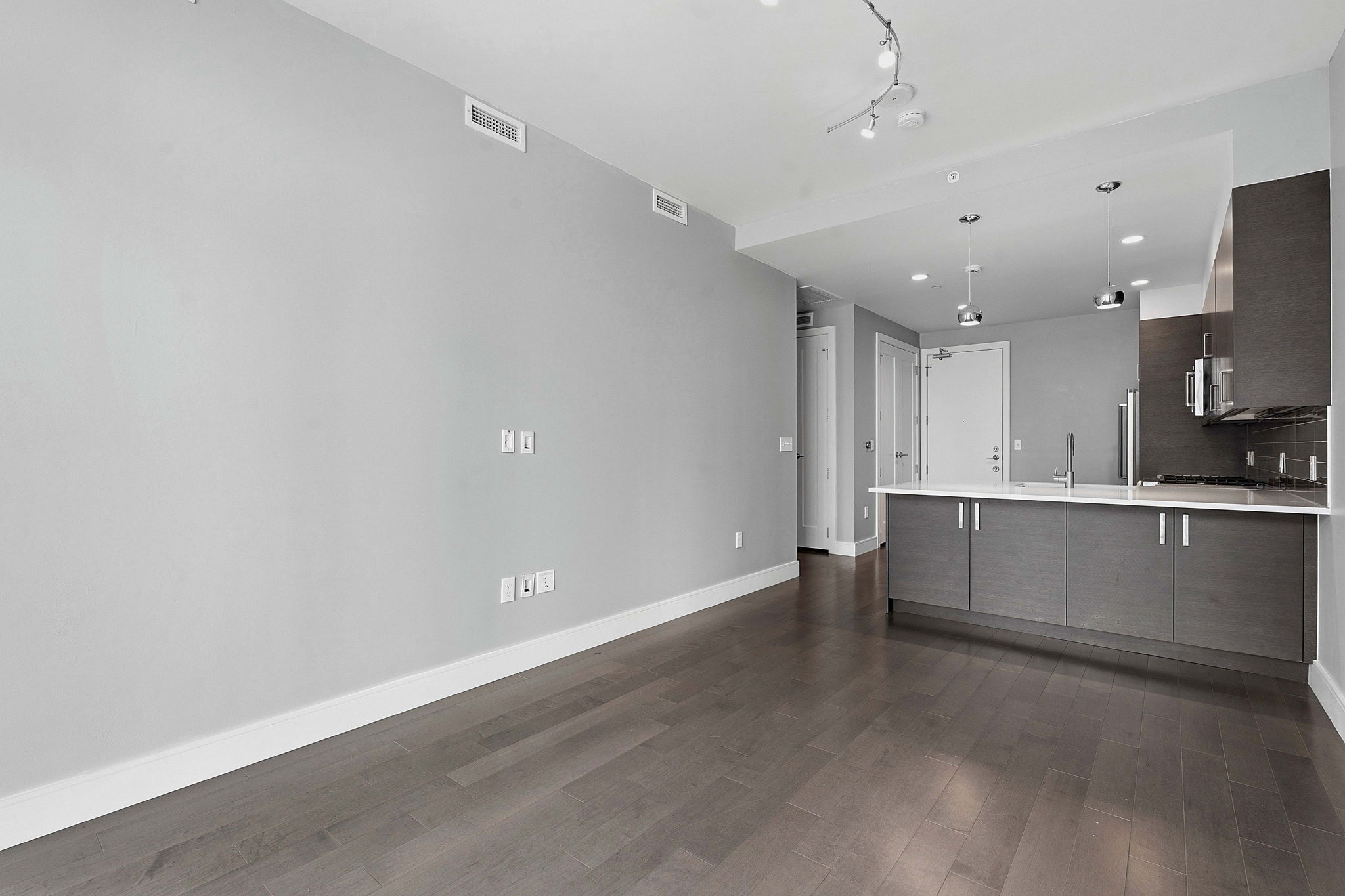 222 West Avenue, Unit 2207 Austin, TX 78701 - Photo 9 of 30 Open-concept living area featuring rich wood-finish flooring, a modern kitchen with grey cabinetry, stainless steel appliances, and a white countertop