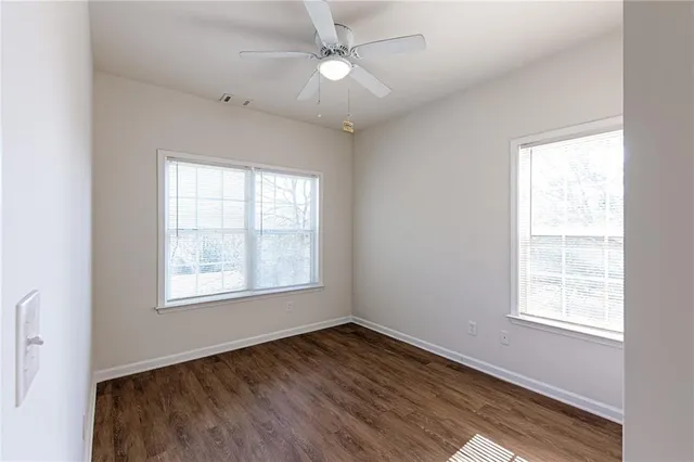 an empty room with wooden floor ceiling fan and windows