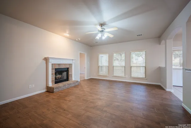 a view of an empty room with chandelier fan and wooden floor