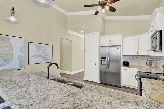 a kitchen with stainless steel appliances granite countertop a refrigerator a stove a sink and white cabinets with wooden floor