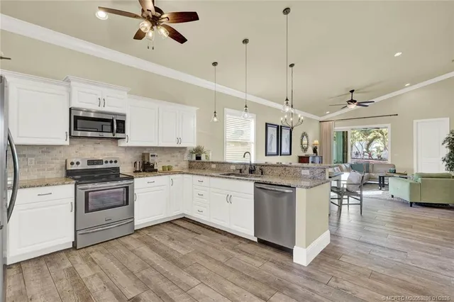 a kitchen with stainless steel appliances granite countertop a refrigerator a sink dishwasher a stove and white countertops with wooden floor