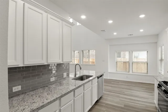 a kitchen with stainless steel appliances granite countertop a stove a sink a refrigerator white cabinets and a refrigerator