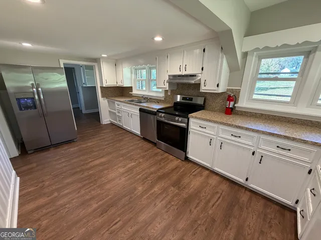 a kitchen with stainless steel appliances granite countertop a refrigerator a sink dishwasher a stove and white countertops with wooden floor