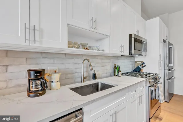 a kitchen with stainless steel appliances granite countertop a stove a sink dishwasher and a refrigerator with white cabinets