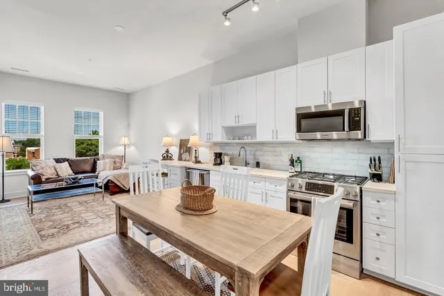 a large white kitchen with stainless steel appliances granite countertop a stove a sink dishwasher a dining table and chairs with wooden floor