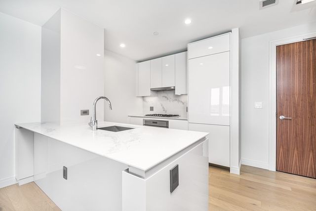 a kitchen with a sink a stove a refrigerator and white cabinets with wooden floor