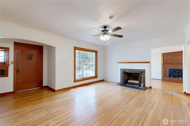 a view of an empty room with wooden floor fireplace and a window