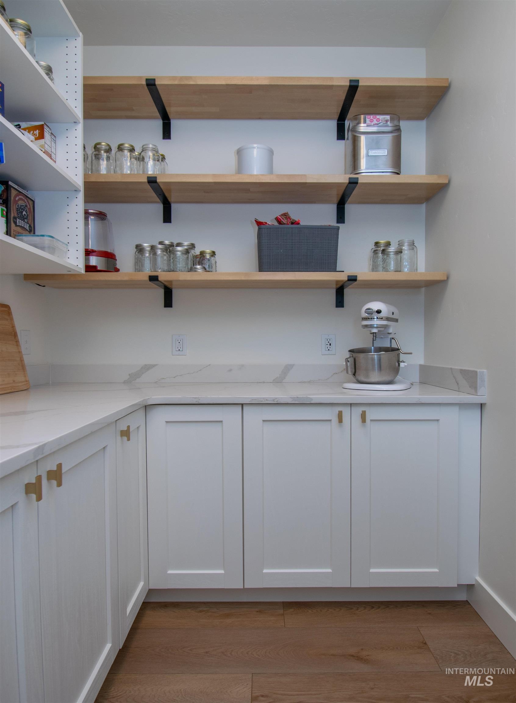 44 Big Moose Road McCall, ID 83638 - Photo 12 of 50 Spacious pantry featuring white shaker-style cabinetry with gold-tone hardware, a white countertop with subtle veining, and open wood shelving with matte black brackets