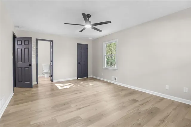 a view of an empty room with wooden floor and a ceiling fan