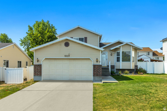 Split-level residence featuring a two-car garage, light-colored siding, and brick accents