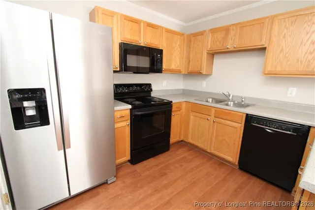 a kitchen with stainless steel appliances a sink a stove a microwave a refrigerator a cabinets and wooden floor