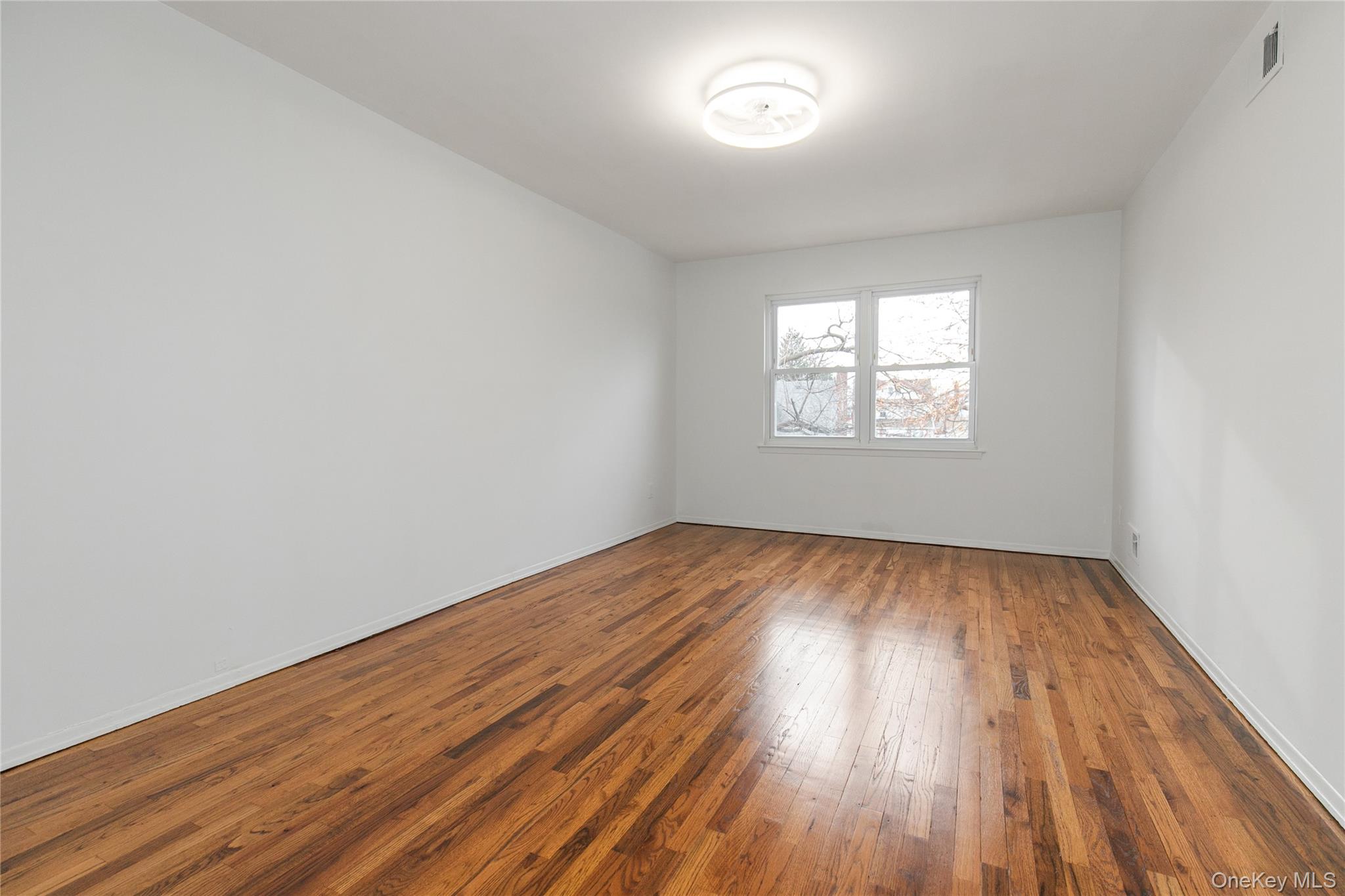 676 Front Street, Unit F Hempstead, NY 11550 - Photo 13 of 18 an empty room with wooden floor and windows
