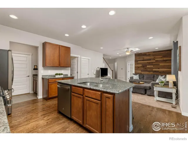 a kitchen with stainless steel appliances granite countertop a stove top oven a sink dishwasher and a refrigerator with wooden floor