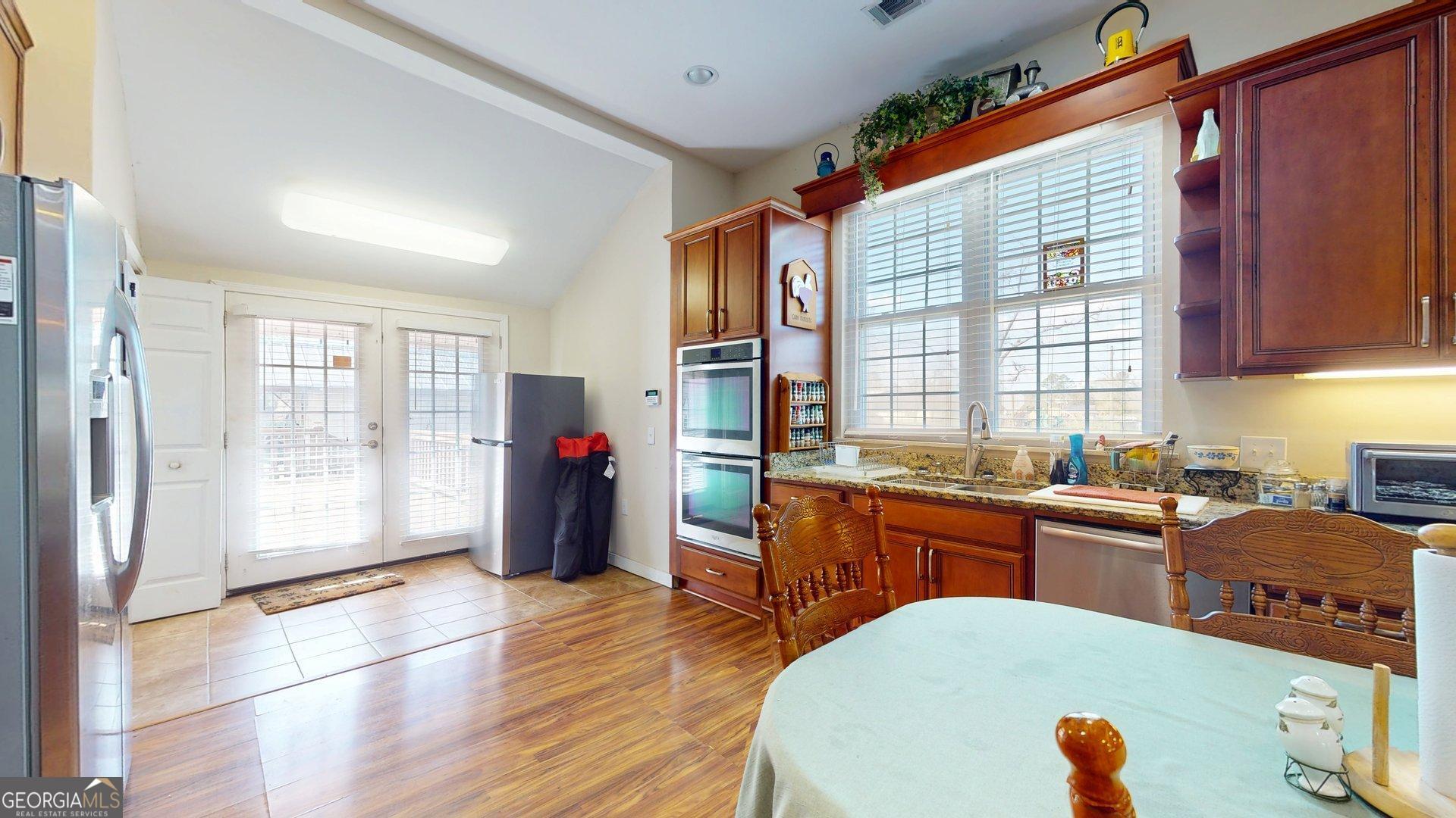 297 North Rountree Street Metter, GA 30439 - Photo 16 of 34 a large kitchen with stainless steel appliances granite countertop a refrigerator a sink dishwasher a dining table and chairs with wooden floor