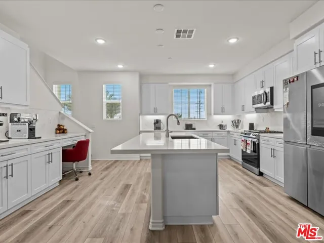 a kitchen with kitchen island a white counter top space a sink stainless steel appliances and cabinets