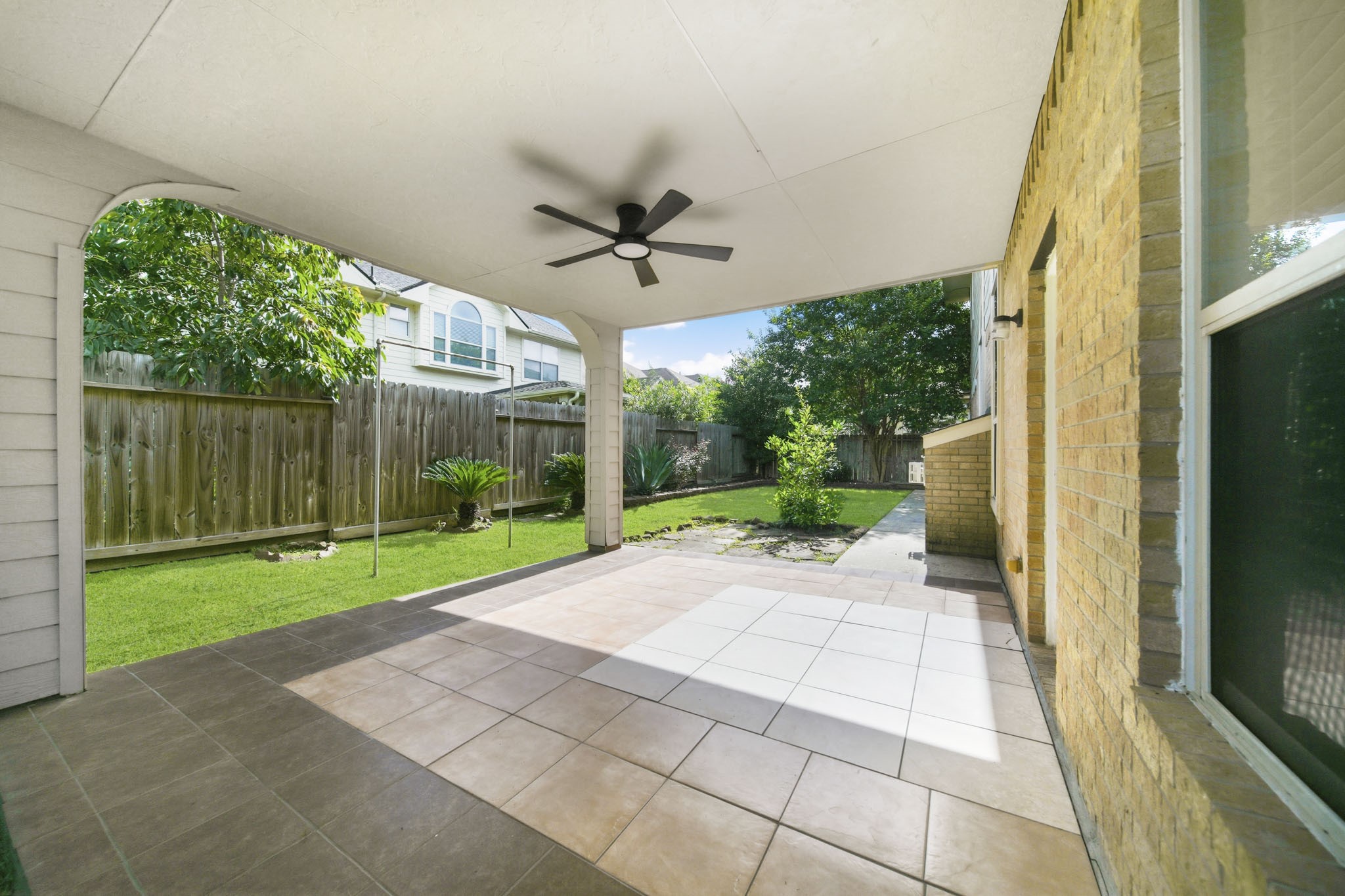 3306 Colleville Sur Mer Lane Spring, TX 77388 - Photo 25 of 30 Step outside to a spacious covered patio designed for year-round outdoor enjoyment. Featuring durable tile flooring, a ceiling fan, and ample room for outdoor seating and dining, this inviting space is perfect for relaxing, entertaining, or hosting weekend gatherings. The patio overlooks a private, fully fenced backyard with lush green space, mature landscaping, and plenty of room for pets, play, or gardening.