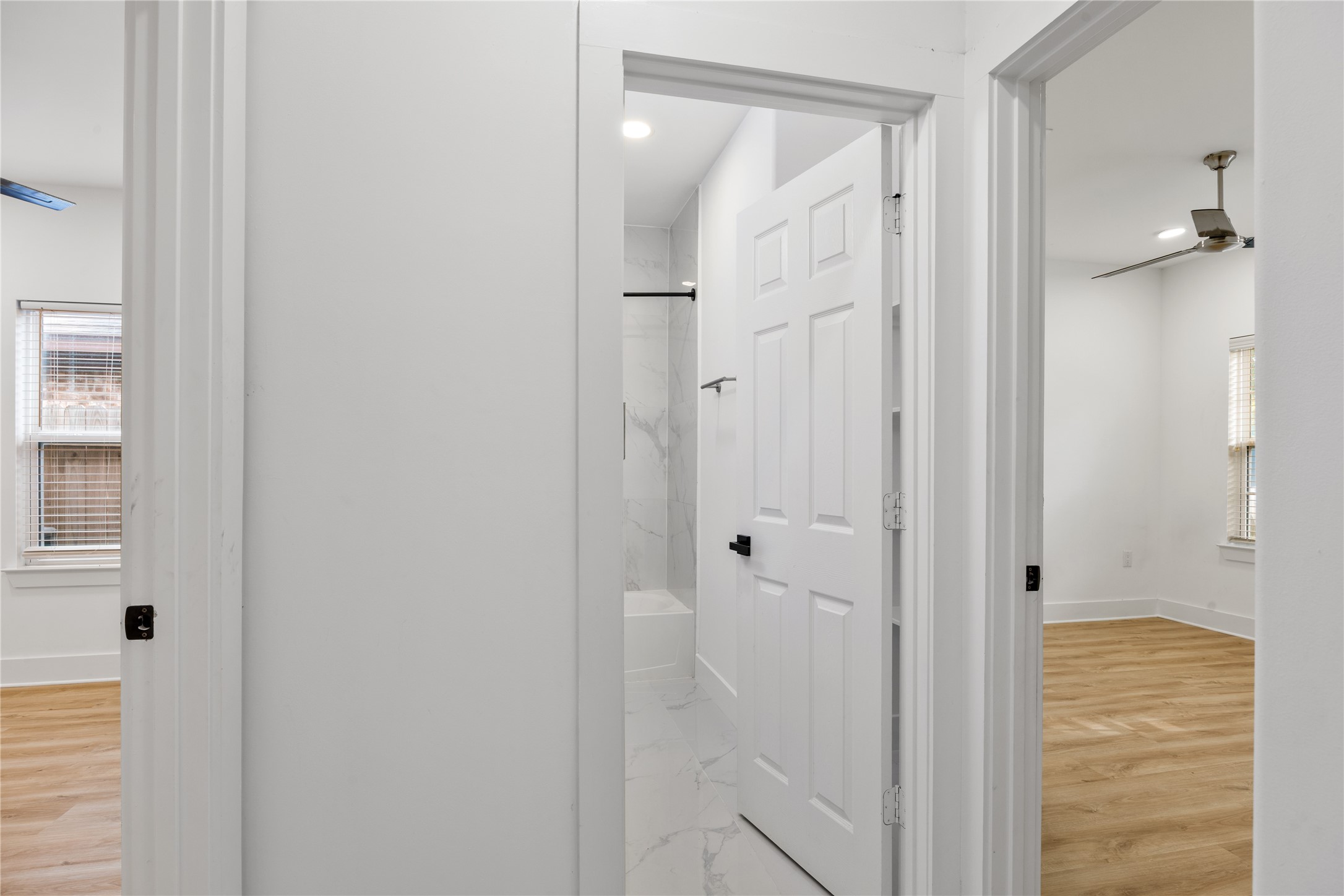 1121 Austin Street Rosenberg, TX 77471 - Photo 6 of 44 This photo shows a hallway with a bathroom and two adjacent rooms. The bathroom features modern white tiles and a bathtub. The rooms have luxury vinyl floors and ceiling fans, creating a bright and inviting space.