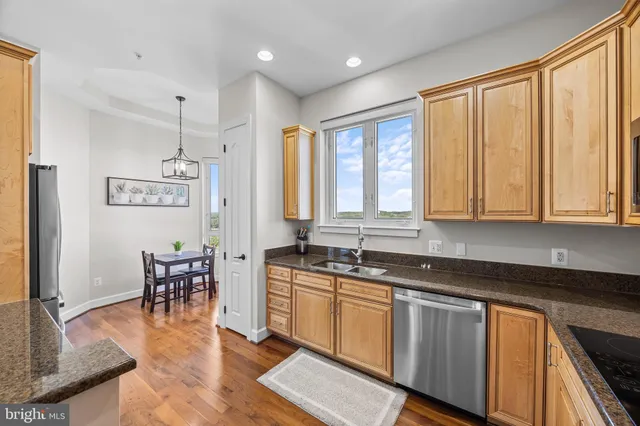 a kitchen with stainless steel appliances granite countertop a stove top oven a refrigerator a dining table and chairs with wooden floor