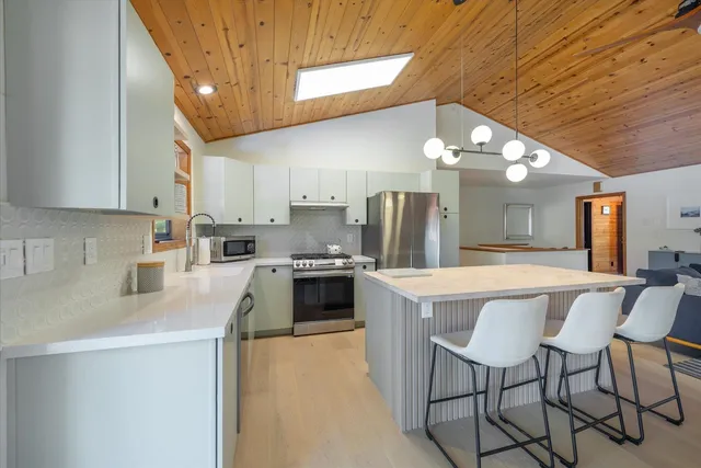 a kitchen with stainless steel appliances a sink a stove a refrigerator cabinets and chairs
