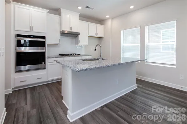 a kitchen with stainless steel appliances granite countertop a stove a sink and white cabinets with wooden floor