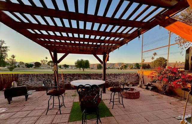 1395 Lause Road Bullhead City, AZ 86442 - Photo 29 of 34 Expansive paver patio with a wooden pergola, brick fire pit, and a low brick wall bordering a green expanse