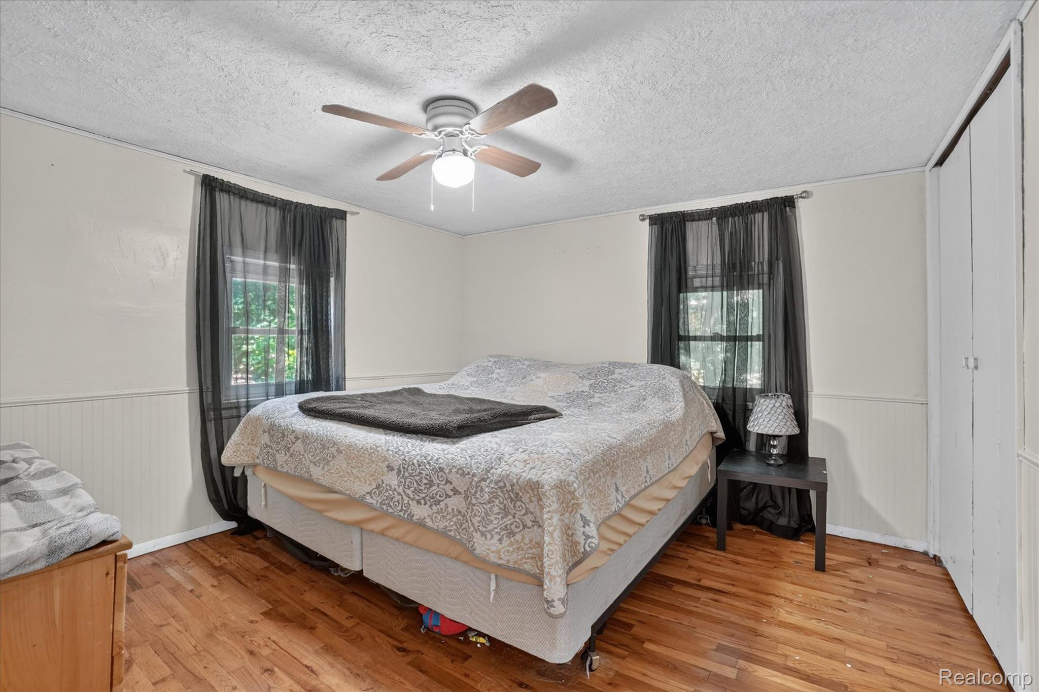 508 Deland Road Flushing, MI 48433 - Photo 17 of 38 Bedroom featuring wood-finish flooring, two windows, wainscoting, a ceiling fan with integrated lighting, and a bi-fold closet