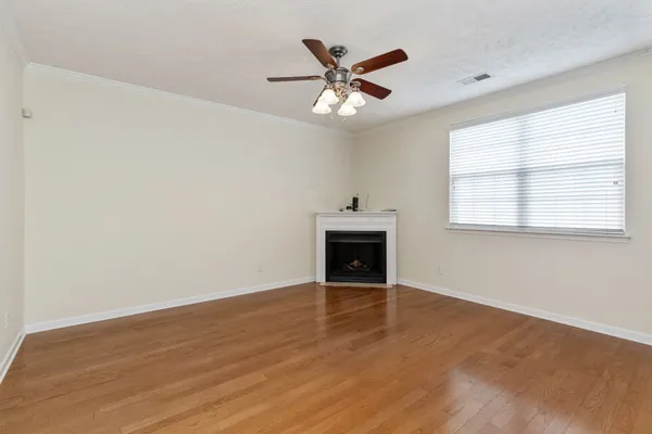 an empty room with wooden floor fan and windows