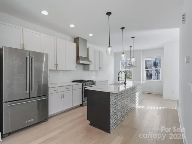 a kitchen with stainless steel appliances granite countertop a refrigerator a sink dishwasher a stove and white cabinets with wooden floor