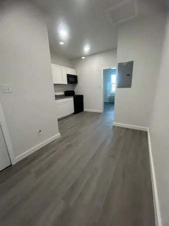 an empty room with wooden floor and kitchen view