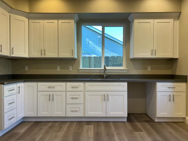 a kitchen with stainless steel appliances granite countertop a sink a stove and white cabinets with wooden floor